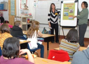 Two teachers present a lesson to students sitting at desks