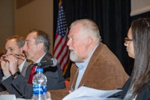 Man speaking into microphone as three other people sitting next to him look on