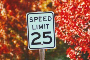 a white speed limit sign with bright colored leaves in the background