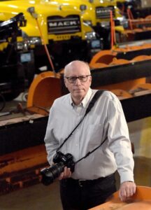 man holding a camera poses in front of snowplows